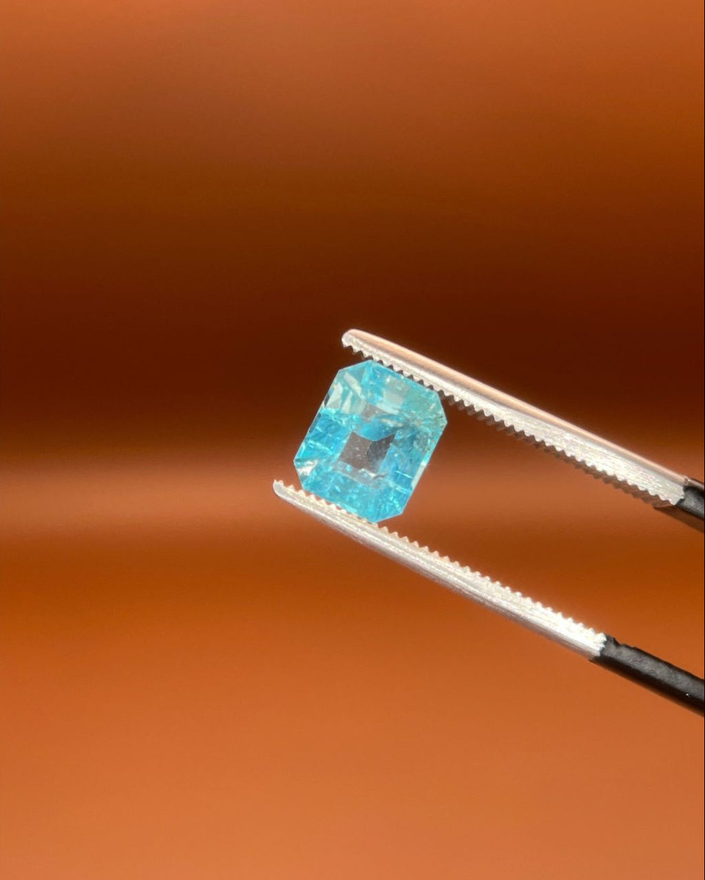 Natural 1.30ct indicolite tourmaline, emerald cut, icy sky-blue, held in gemologist tweezers