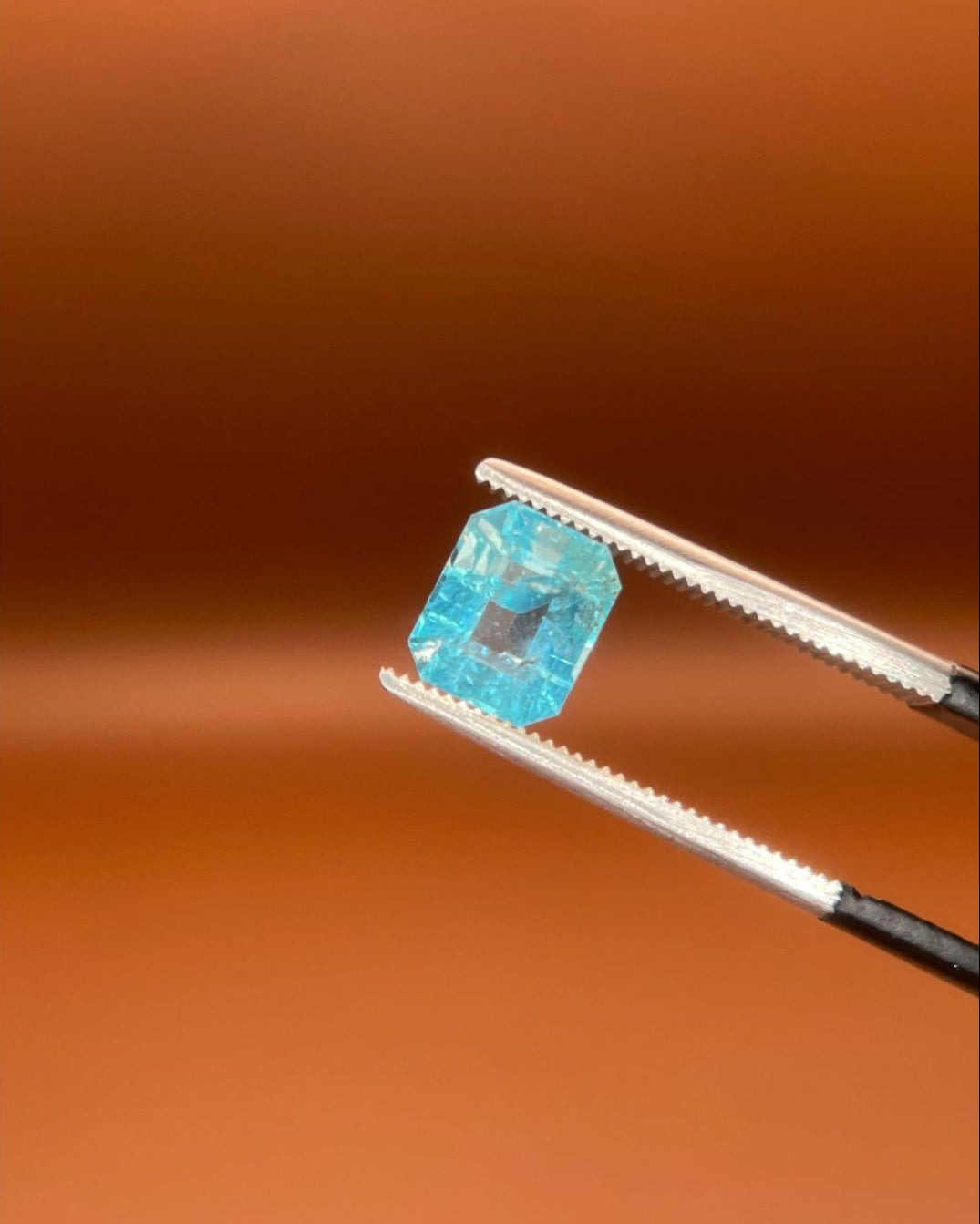 Natural 1.30ct indicolite tourmaline, emerald cut, icy sky-blue, held in gemologist tweezers