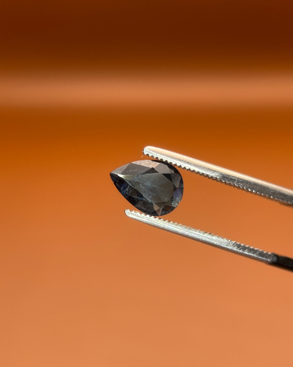 Natural 0.80ct indicolite tourmaline, pear cut, midnight blue, held in gemologist tweezers