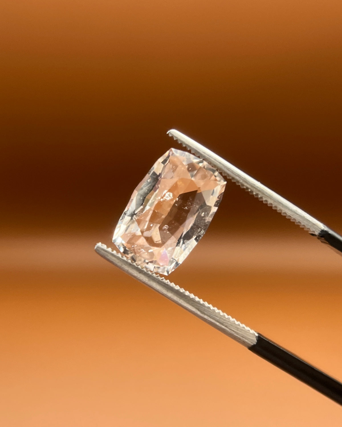 Natural 3.85ct imperial topaz, cushion cut, soft peach-gold, held in gemologist tweezers